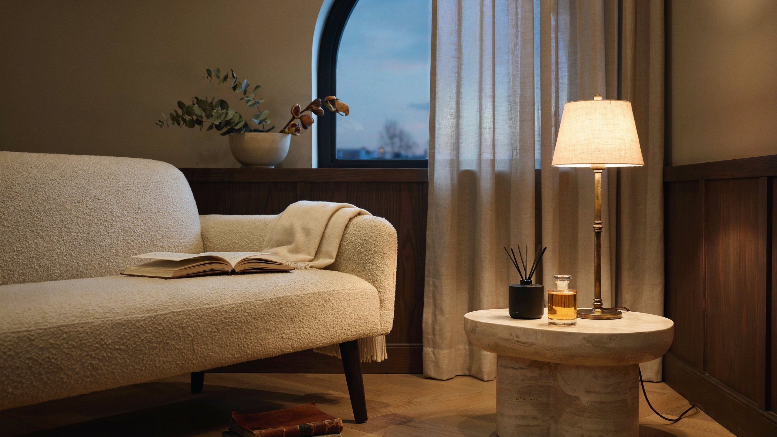 Warm hotel-inspired lounge with home-fragrance details beside a lamp.